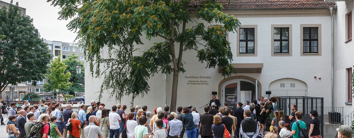 Menschen stehen vor einem weißen Gebäude mit der Aufschrift "Kunsthaus Dresden"