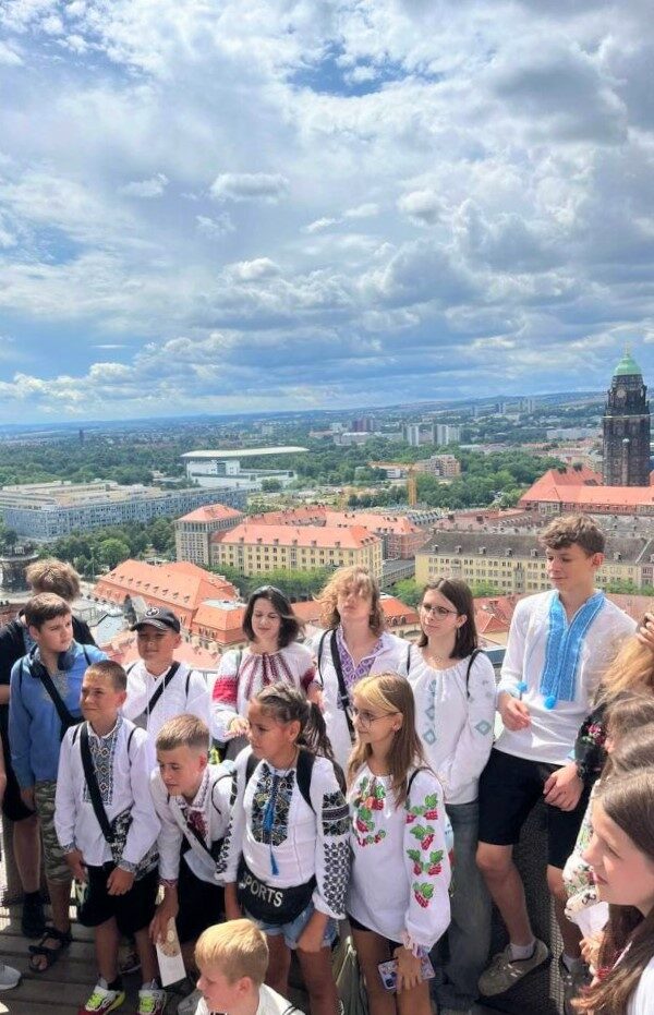 Eine Gruppe Jugendlicher steht auf dem Turm der Frauenkirche. Im Hintergrund sieht man die Sicht über Dresden und den Dresdner Rathausturm
