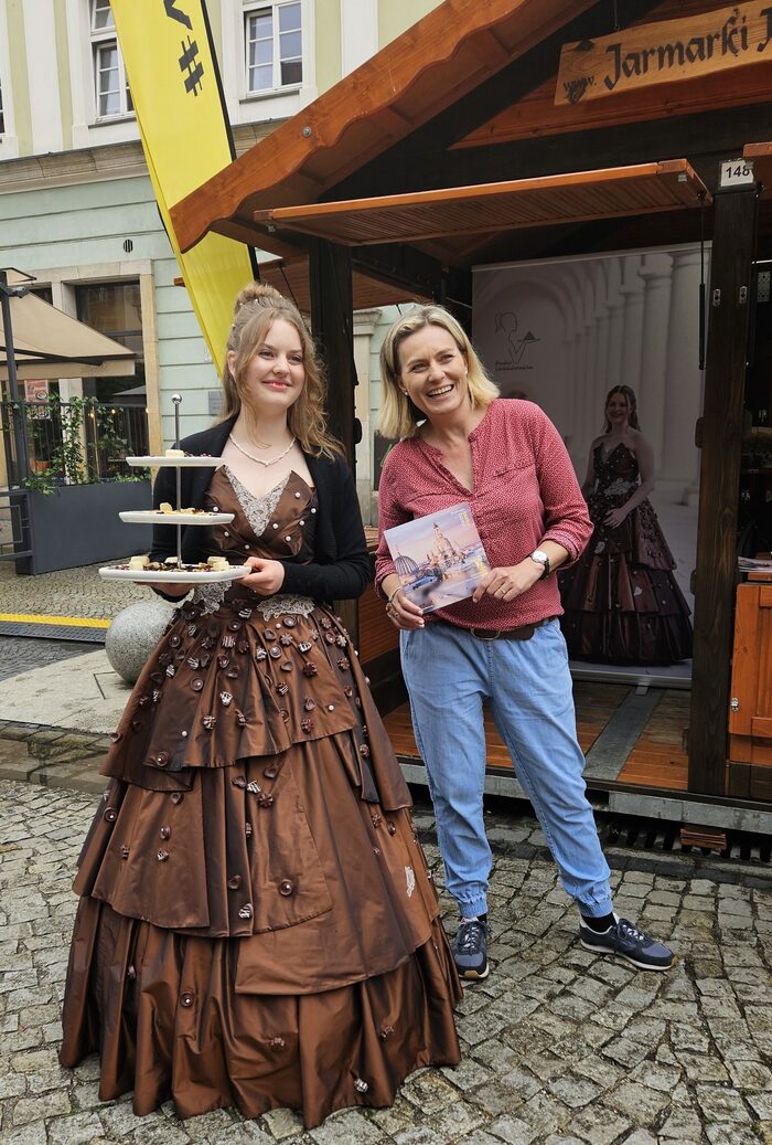 Das Dresdner Schokoladenmädchen und eine Mitarbeiterin der Stadt Dresden stehen nebeneinander auf vor dem Marktstand
