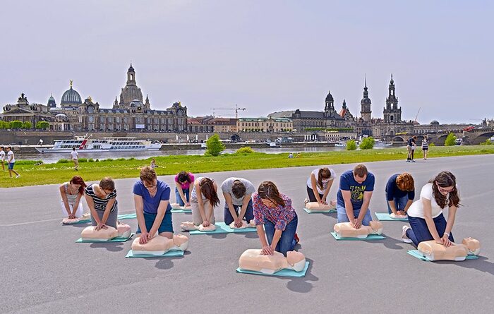 Eine Gruppe junger Menschen übt die Reanimation an Puppen von der Stadtsilhouette von Dresden