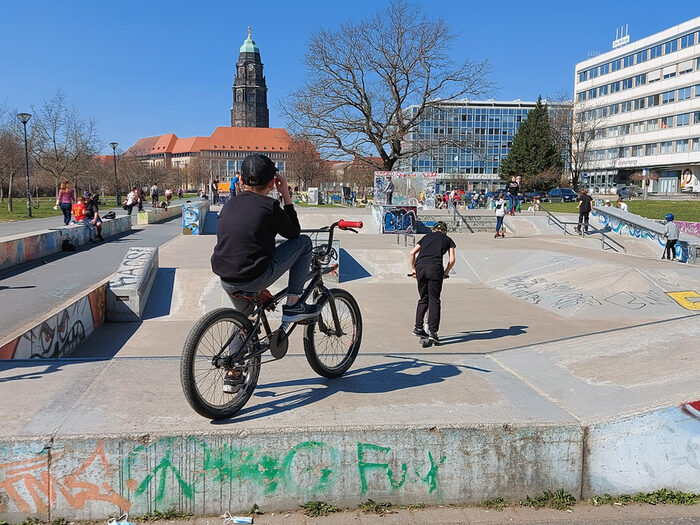 Auf der Skateanlage sind bei schönem Wetter viele Kinder und jugendliche mit Bikes und Skateboards aktiv. Im Hintergrund das Rathaus mit dem Rathausturm.