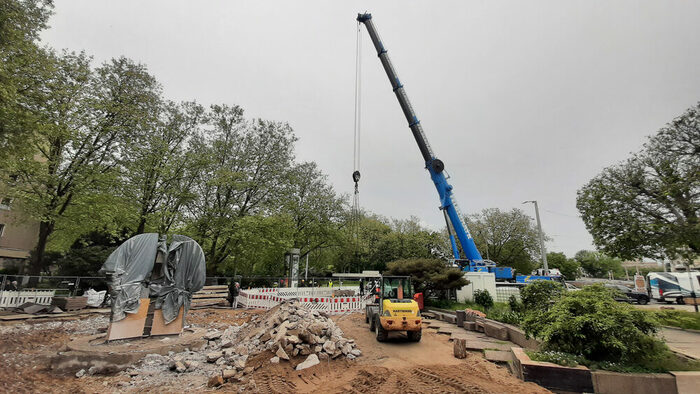 Brunnenbaustelle Mai 2024 beim Einbau der Brunnenstube, links die Brunnenskulptur im ehemaligen Brunnenbecken, rechts Kran und Radlader