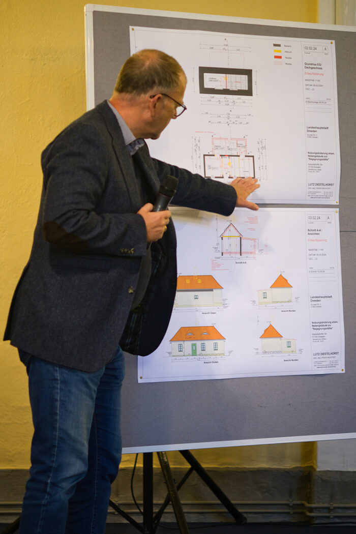 Der Architekt Lutz Diestelhorst stellte die Vorplanung für die Sanierung des ehemaligen Verwalter-Häuschens vor. Er erklärt, indem er auf einer technischen Zeichnung das Projekt zeigt. Die Zeichnung ist auf einer Pinnwand befestigt.