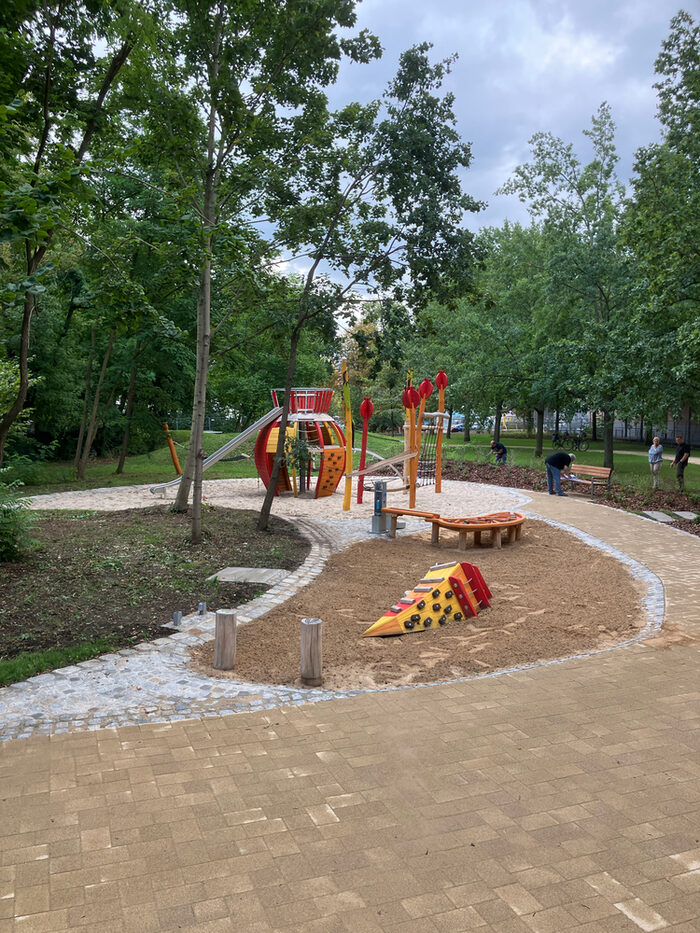 Park an der Haydnstraße_Spielplatz zur Bauabnahme. Spielgeräte in einer Sandfläche, ringsum neu gebaute Pflasterwege und Pflanzflächen