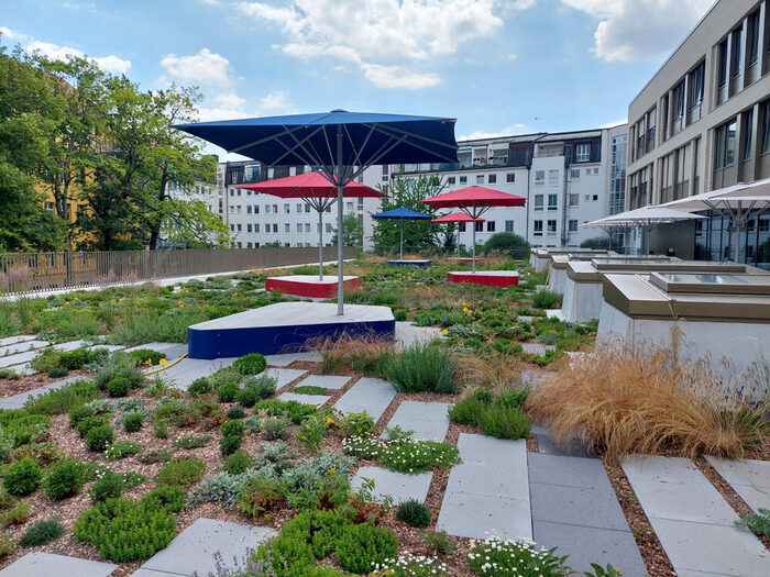 Berufsschulzentrum "Prof. Dr. Zeigner": fertiggestellte Außenanlagen mit roten und blauen Sonnenschirmen im Hofbereich, eingerahmt von Gebäuden und Bäumen