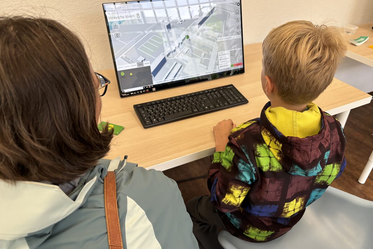 Eine Frau und ihr Sohn von hinten, die auf einen Monitor schauen.