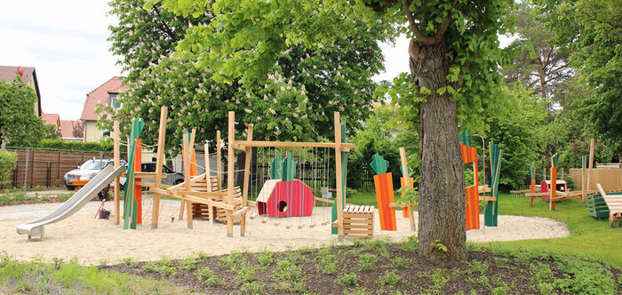 Spielplatz mit verschiedenen Spielgeräten, Bäumen und Wiese