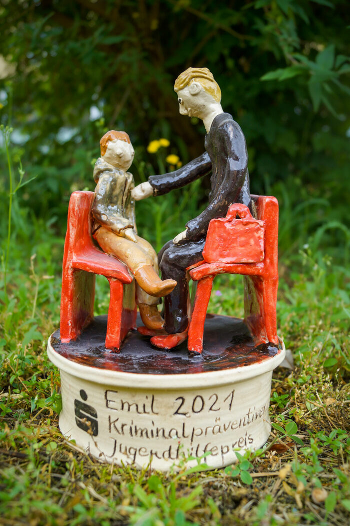 EMIL 2021 – kriminalpräventiver Jugendhilfepreis; Skulptur, Kind und Mann auf roten Stühlen