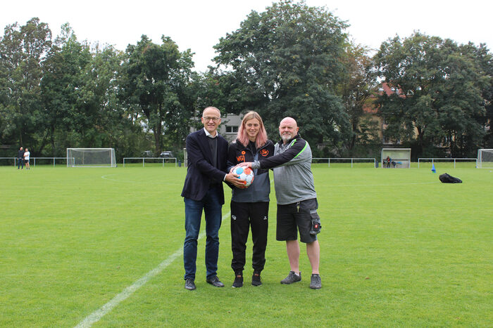 Sportbürgermeister Dr. Peter Lames mit Anne Waldhauer, längste aktive Spielerin beim SV Johannstadt 90 e. V., und Uwe Herrmann, 2. Vorsitzender und Abteilungsleiter Frauenfußball, auf dem Fußballfeld, halten einen Fußball