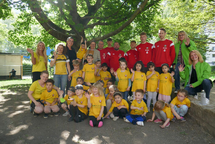 Gruppenbild: Kinder und Erzieherinnen aus der städtischen Kita Hopfgartenstraße 9, Frau Bibas, Spieler und Trainer von Dynamo Dresden sowie Mitarbeiterinnen der AOK Plus