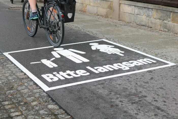 Ein Piktogramm von einem Radfahrenden und einer Person mit Kind auf dem Elberadweg mit "Bitte langsam"-Aufschrift.