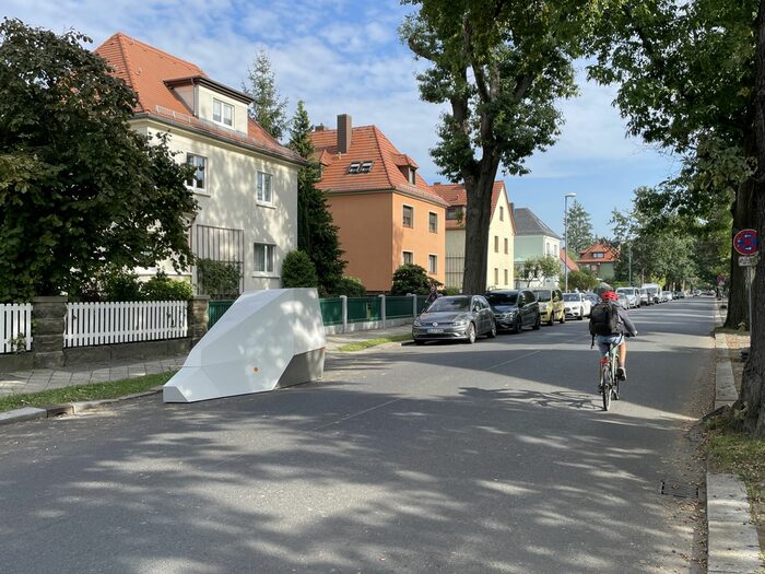 Ein mobiler Blitzer steht auf einer Straße, im Vordergrund fährt ein Radfahrer vorbei, im Hintergrund stehen Häuser