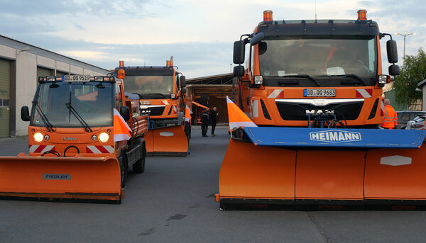 Drei orangefarbene Fahrzeuge mit Schneeschiebern vorn