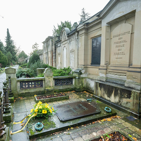 Gruft, auf der ein Kranz mit gelben Blumen liegt