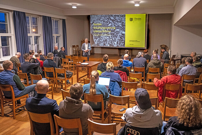 Zu sehen ist Herr Kühn (Baubürgermeister) sowie weitere Referenten und das Publikum zur Info-Veranstaltung Soziale Erhaltungssatzungen in Dresden am 1.3.2024 im Gemeindesaal der Hoffnungskirche.