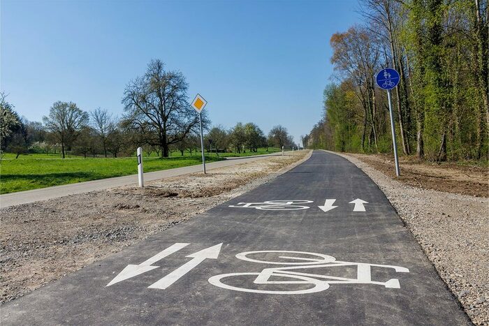 Auf einem Schild ist ein gemeinsamer Fuß- und Radweg ausgewiesen, im Hintergrund ein Radfahrer.