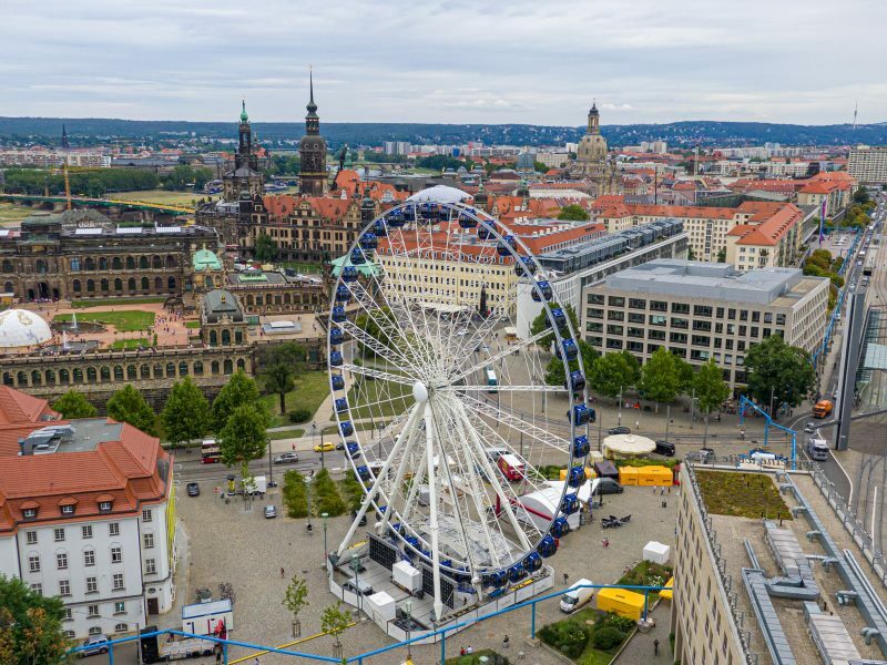Luftaufnahme des Riesenrades „Wheel of Vision“ auf dem Dresdner Postplatz. Im Hintergrund sind einige der Sehenswürdigkeiten wie der Zwinger und die Frauenkirche zu sehen.